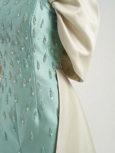 تسوقي فستان سهرة تفته أمريكي يدمج اللونين التركواز والبيج، يتميز بأكتاف فراشة مزمومة وقصة مخصرة لإطلالة ملكية.